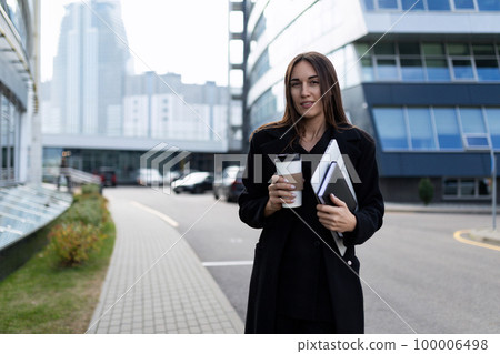 a successful woman investor stands against the backdrop of a business building holding a cup of a successful woman investor stands against the backdrop of a business building holding a cup of 100006498