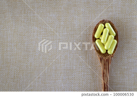 Capsules yellow Quercetin in a wooden spoon on a beige background. Top view, copy space. 100006530
