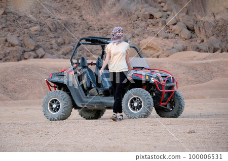 Young woman was riding a buggy. Walks away from him in the desert and looks away. 100006531