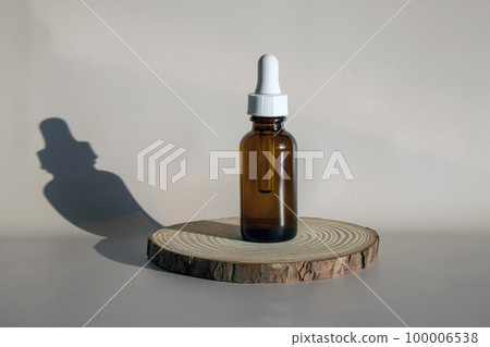 Mock-up of a brown glass bottle with an eyedropper. Serum or oil for face and body. Round wooden podium on beige background. Mock-up of a brown glass bottle with an eyedropper. Serum or oil for face and body. Round wooden podium on beige background. 100006538