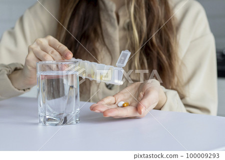 A woman pours pills into her hand from a medical organizer container. Daily intake of medicines and pills. A woman pours pills into her hand from a medical organizer container. Daily intake of medicines and pills. 100009293