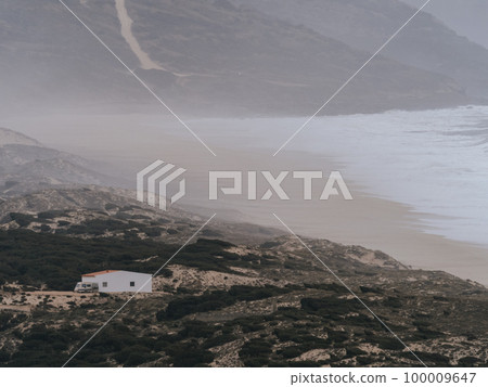 A serene and tranquil scene featuring a solitary house standing on the shores of the Atlantic Ocean in Portugal. The subdued colors and misty atmosphere created by the crashing waves provide a feeling A serene and tranquil scene featuring a solitary house standing on the shores of the Atlantic Ocean in Portugal. The subdued colors and misty atmosphere created by the crashing waves provide a feeling 100009647