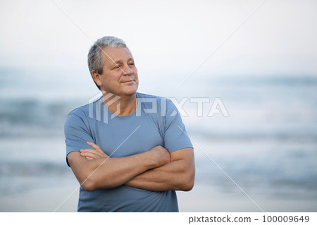 Middle shot of a smiling senior man looking away with arms crossed on the chest. Cheerful person on blurry background of sea and sky Middle shot of a smiling senior man looking away with arms crossed on the chest. Cheerful person on blurry background of sea and sky 100009649