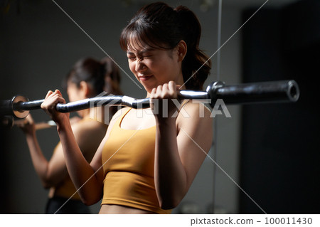 Young woman training with barbell shaft 100011430
