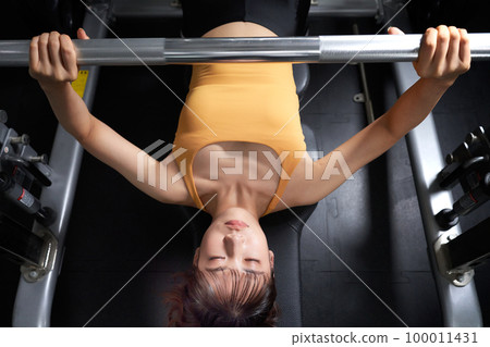 Young woman doing strength training with bench press at the gym 100011431