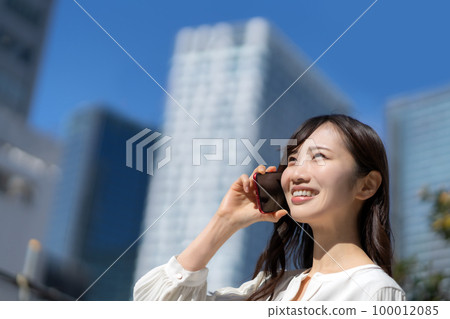 A young woman talking on a smartphone with the blue sky in the background 100012085
