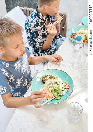 Hungry boys eat delicious dinner sitting at table in restaurant closeup. Preteen children enjoy fresh healthy food in cozy cafeteria 100013512
