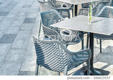 Comfortable plastic chairs and porcelain stoneware table with flower in glass vase on city street closeup. Furniture for restaurants and cafes 100013557