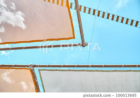 Canopy and rope bridge in recreational area of water park against clear blue sky. Orange sun-protection cover above deck chairs closeup 100013695