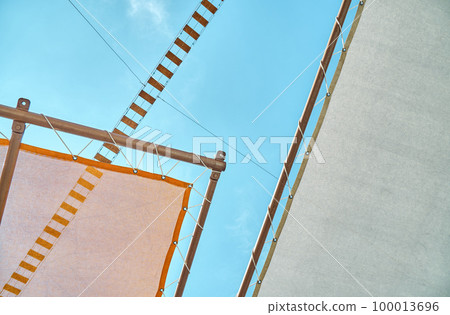 Canopy and rope bridge in recreational area of water park against clear blue sky. Orange sun-protection cover above deck chairs closeup Canopy and rope bridge in recreational area of water park against clear blue sky. Orange sun-protection cover above deck chairs closeup 100013696
