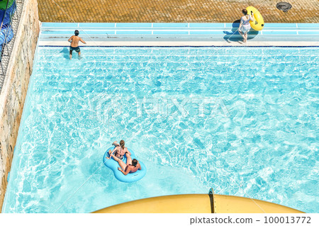 People relax on inflatable rubber rings in swimming pool with clear blue water. Fun activities in water park at summer resort upper view People relax on inflatable rubber rings in swimming pool with clear blue water. Fun activities in water park at summer resort upper view 100013772
