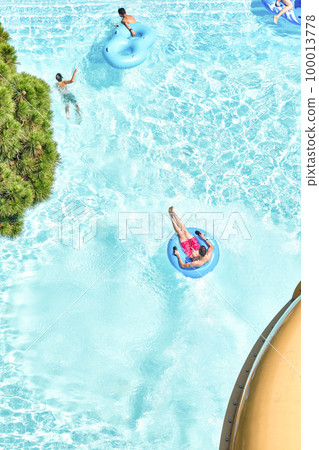 People relax on inflatable rubber rings in swimming pool with clear blue water. Fun activities in water park at summer resort upper view People relax on inflatable rubber rings in swimming pool with clear blue water. Fun activities in water park at summer resort upper view 100013778