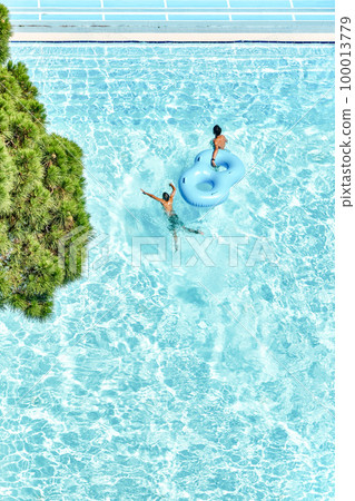 People relax on inflatable rubber rings in swimming pool with clear blue water. Fun activities in water park at summer resort upper view 100013779