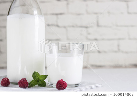 Organic probiotic milk kefir drink or yogurt in glass containers, with raspberry, on the white grey background. Gut health. Probiotic cold fermented dairy drink. Trendy food and drink. Copy space Organic probiotic milk kefir drink or yogurt in glass containers, with raspberry, on the white grey background. Gut health. Probiotic cold fermented dairy drink. Trendy food and drink. Copy space 100014802