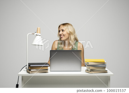 Portrait of a pretty young woman studying while sitting at the table with grey laptop computer, notebook. Smiling business woman working with a laptop isolated on a grey background. Portrait of a pretty young woman studying while sitting at the table with grey laptop computer, notebook. Smiling business woman working with a laptop isolated on a grey background. 100015537