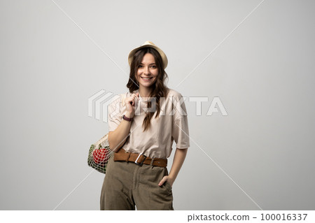 Woman in a beige t-shirt and a hat holding mesh shopping bag with groceries. Conscious consumption. Eco trend. Zero waste concept. Girl carry bag shopper. Woman in a beige t-shirt and a hat holding mesh shopping bag with groceries. Conscious consumption. Eco trend. Zero waste concept. Girl carry bag shopper. 100016337
