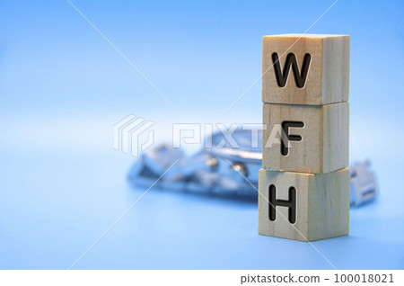 WFH text represent work from home text engraved on wooden blocks with light blue and watch background. Work from home concept. Copy space. 100018021