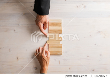 Male and female hands pushing two blank wooden pegs into a stack of them Male and female hands pushing two blank wooden pegs into a stack of them 100020073