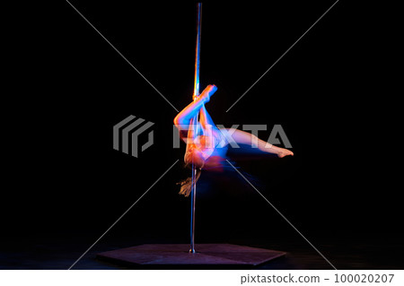 Passionate hobby. Young artistic girl performing pole dance isolated over black studio background with mixed neon lights. Concept of art, sport and modern dance 100020207