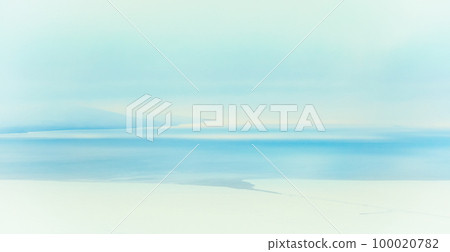 Blurry winter snow background. Winter seascape. Icy shore and ice-covered sea bay. Freezing water. Snow and ice on the coast. Mountains in the distance. 100020782