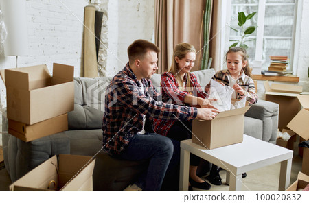Putting things on place. Young happy family, man, woman and kid moving into new flat, apartment with many cardboard boxes 100020832