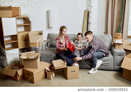 Young happy family, man, woman and kid, daughter moving into new flat, apartment with many cardboard boxes filled with clothes Young happy family, man, woman and kid, daughter moving into new flat, apartment with many cardboard boxes filled with clothes 100020852