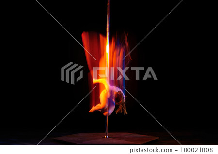 Young athletic girl dancing on pylon, performing pole dance isolated over black studio background with mixed neon lights. Concept of art, sport and modern dance 100021008