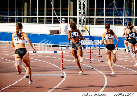 women running 400 - meter hurdles in athletics competition 100022247