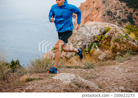 male runner running on mountain trail along sea 100022273