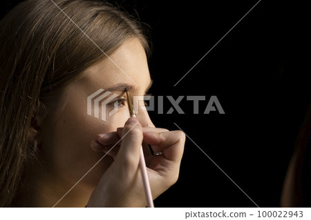 Makeup artist doing a eyebrows makeup on a beautiful woman face. Hand of make-up master is painting eyebrow of young beauty model girl. Make up in process. Makeup artist doing a eyebrows makeup on a beautiful woman face. Hand of make-up master is painting eyebrow of young beauty model girl. Make up in process. 100022943