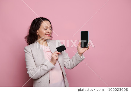 Pretty woman in formal suit, confident successful business lady, entrepreneur, sales manager or bank client, smiling and showing at camera a black credit card and smartphone, on isolated background Pretty woman in formal suit, confident successful business lady, entrepreneur, sales manager or bank client, smiling and showing at camera a black credit card and smartphone, on isolated background 100025608