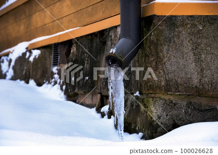 icy drainpipe near the stone foundation of an old house 100026628