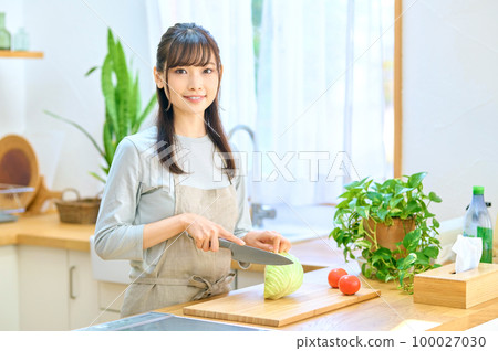 Young housewife in an apron cooking in the kitchen Young housewife in an apron cooking in the kitchen 100027030