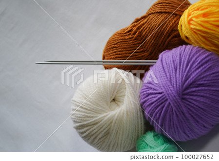 Knitting needles and skeins of yarn on white background. Multicolored balls of acrylic and woolen yarn with knitting needles sticking out of them, as if rolling down the wall. Close-up, copy space. 100027652