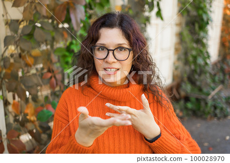 Happy curly woman blogger smiling face talking to webcam recording vlog. Social media influencer woman streaming making video call at outdoor. Headshot portrait selfie webcamera view 100028970