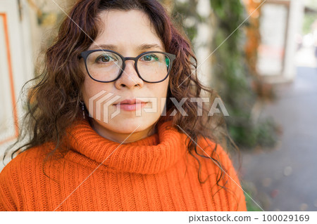 Portrait of carefree young woman smiling with urban background. Cheerful latin girl wearing eyeglasses in the city. Happy brunette woman with curly hair and spectacles smiling. Copy space and empty 100029169