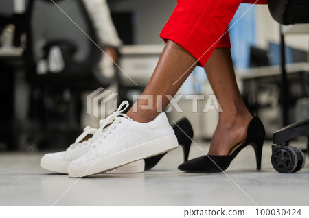 African woman changing from high heels to sneakers in the office. Tired legs. African woman changing from high heels to sneakers in the office. Tired legs. 100030424
