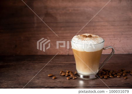 Glass cup of layered coffee drink with milk foam, wooden background and copy space Glass cup of layered coffee drink with milk foam, wooden background and copy space 100031079