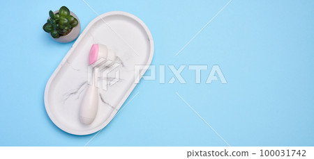 White plastic face scrub brush on a blue background, cosmetic tool. Top view White plastic face scrub brush on a blue background, cosmetic tool. Top view 100031742