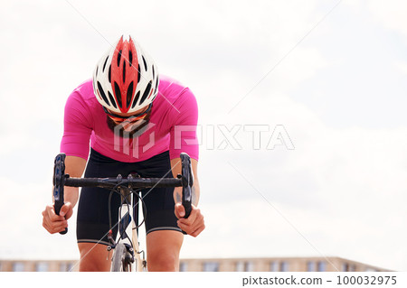 Portrait of a professional cyclist in sportswear, a protective helmet and goggles in a pink jersey against the blue sky, copies. The concept of an active and healthy lifestyle. Portrait of a professional cyclist in sportswear, a protective helmet and goggles in a pink jersey against the blue sky, copies. The concept of an active and healthy lifestyle. 100032975