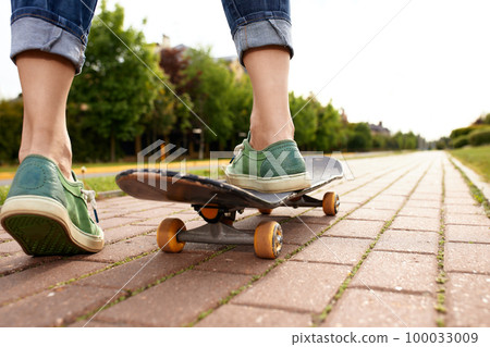 Feet on a skateboard board, rear view shot of feet with sneakers pushing a skateboard in the park, city subculture lifestyle 100033009
