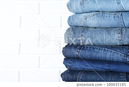 Stack of different jeans near white brick wall, closeup. Space for text Stack of different jeans near white brick wall, closeup. Space for text 100035185
