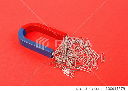 Magnet attracting paper clips on red background Magnet attracting paper clips on red background 100035279