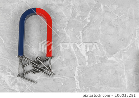 Magnet attracting nails on grey marble table, flat lay. Space for text 100035281