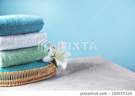 Wicker tray with folded bath towels and beautiful flower on grey table. Space for text Wicker tray with folded bath towels and beautiful flower on grey table. Space for text 100035329