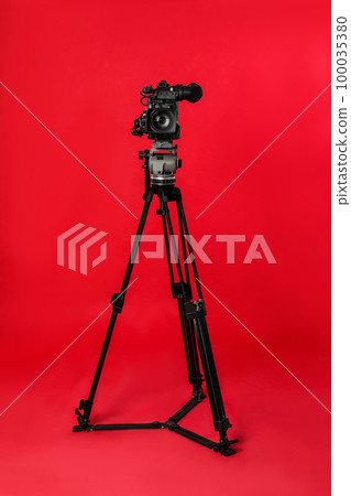 Modern professional video camera on red background 100035380