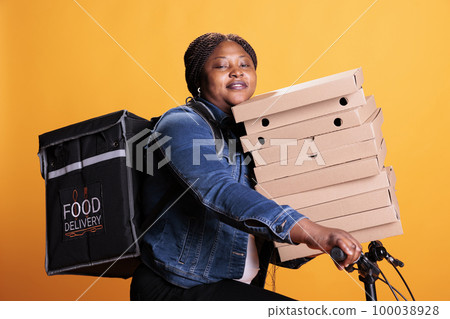 Pizzeria delivery worker carrying stack of cardboard full with pizza delivering takeaway food order to customer during lunch time, standing in studio. Restaurant employee using bike as transportation Pizzeria delivery worker carrying stack of cardboard full with pizza delivering takeaway food order to customer during lunch time, standing in studio. Restaurant employee using bike as transportation 100038928