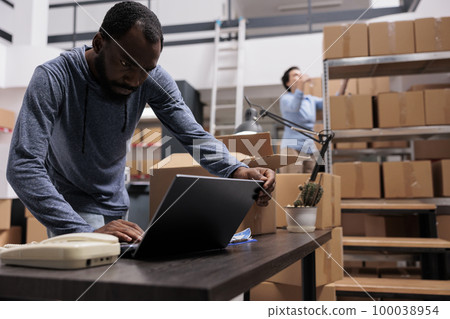 African american supervisor looking at cargo stock on laptop computer before start preparing customers orders, working in warehouse delivery department. Worker checking shipping detalies African american supervisor looking at cargo stock on laptop computer before start preparing customers orders, working in warehouse delivery department. Worker checking shipping detalies 100038954