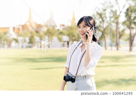 Portrait beautiful young asian woman with smartphone on summer holiday vacation trip with the grand palace in a background at Bangkok, Thailand Portrait beautiful young asian woman with smartphone on summer holiday vacation trip with the grand palace in a background at Bangkok, Thailand 100041295