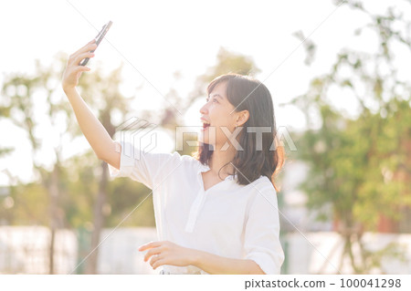 Portrait beautiful young asian woman with smart mobile phone around outdoor nature view in a sunny summer day Portrait beautiful young asian woman with smart mobile phone around outdoor nature view in a sunny summer day 100041298